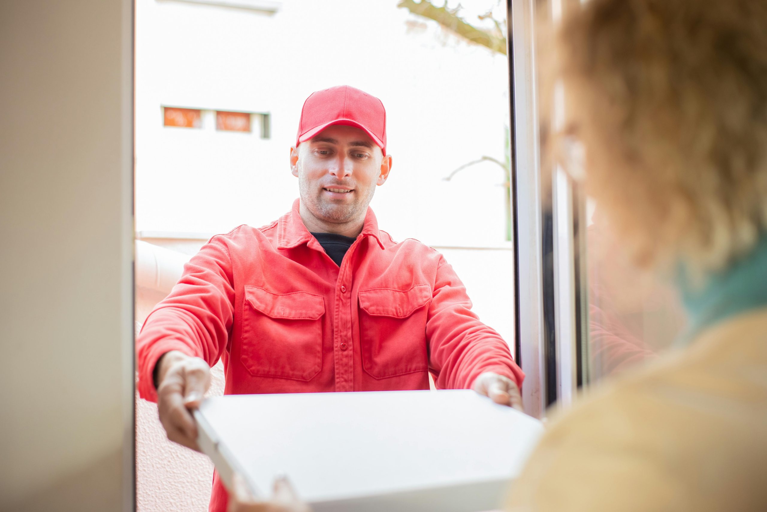 A delivery person in red uniform handing over a package at a doorway.